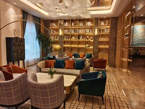 A modern lounge area with a central seating arrangement, a bookshelf, and a decorative ceiling light.