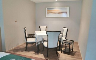 A dining area with a table and four chairs, a painting on the wall, and a wooden floor.