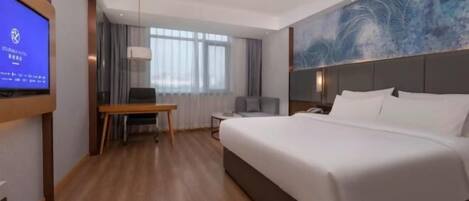 A hotel room with a large bed, a desk, a chair, a TV, and a window with curtains.