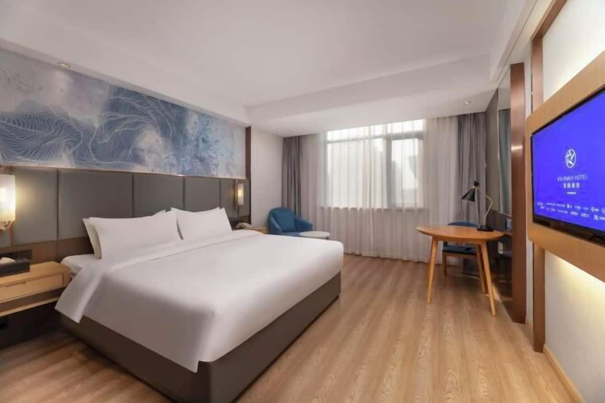 A modern hotel room with a large bed, a desk, a chair, and a television.