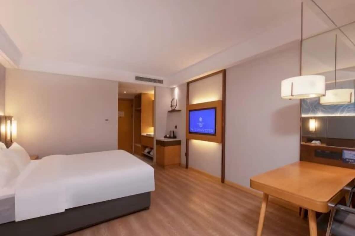 A hotel room with a bed, a desk, a television, and a mirror.