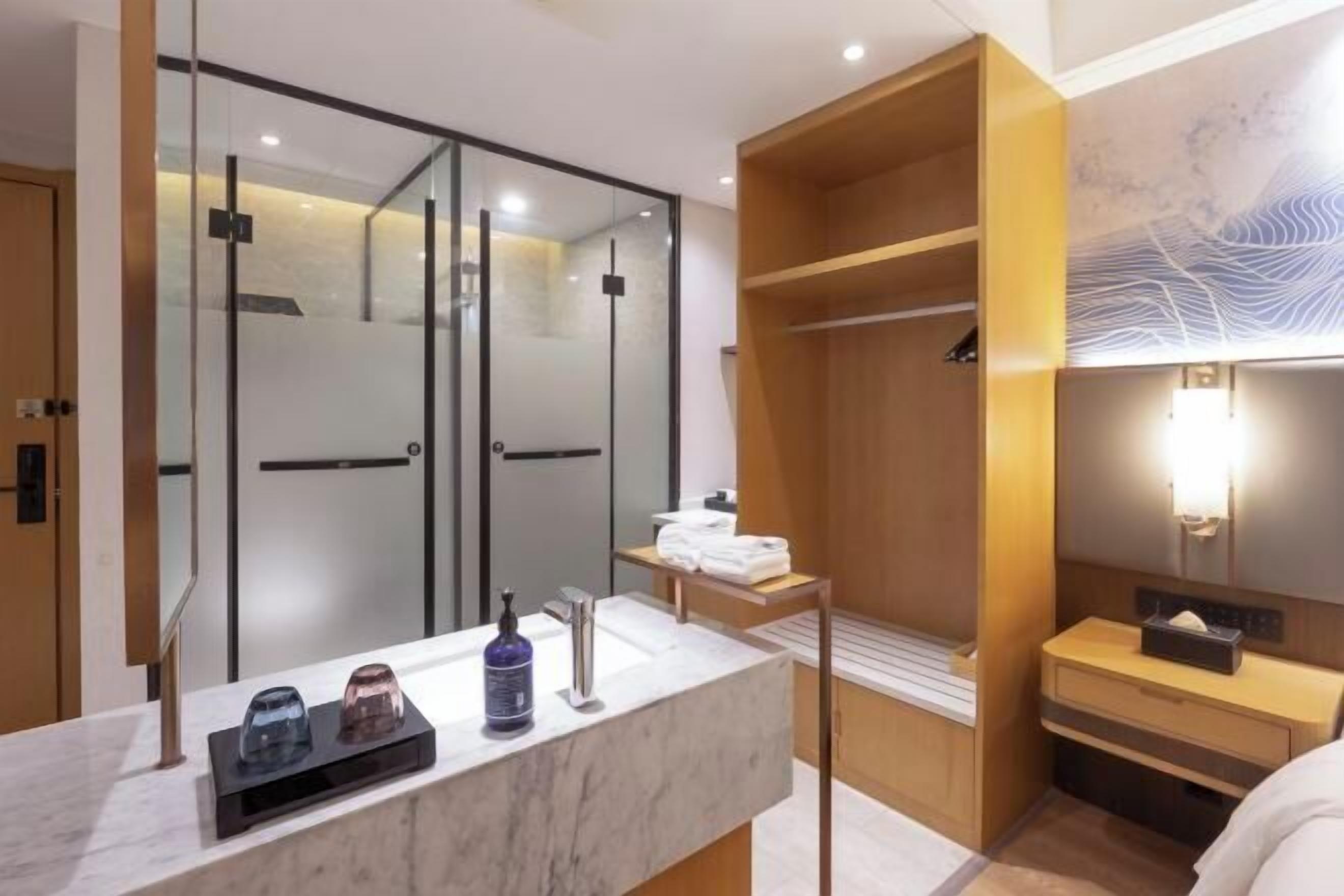 Un baño moderno con cabina de ducha de vidrio, lavamanos de mármol y tocador de madera.
