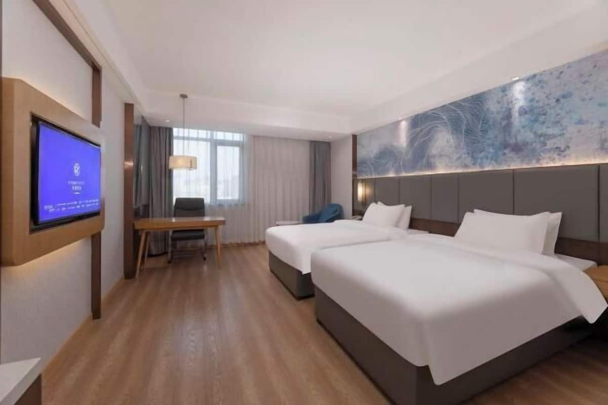 A hotel room with two beds, a desk, a TV, and a large abstract wall art piece.
