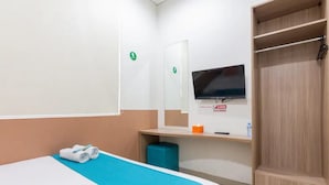 Quarto de hotel com cama, televisão, espelho, guarda-roupa e uma pequena mesa com uma garrafa e uma caixa.