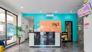 Uma área de recepção de hotel com design moderno, apresentando um balcão de atendimento, um relógio e uma tela de televisão.