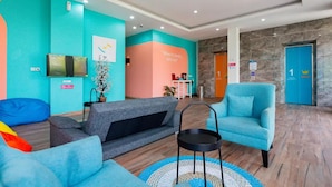 Um hall com paredes verde-água e pêssego, um sofá cinzento, uma poltrona azul, uma mesa pequena e um balcão de recepção.
