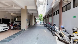 Corredor com carros e motocicletas estacionados, piso de azulejos e um edifício com janelas e placas.