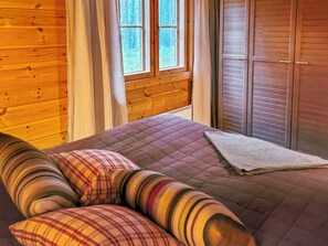Une chambre à coucher avec une tête de lit en bois, un lit recouvert d’une courtepointe, une fenêtre avec des rideaux et une armoire à portes coulissantes.