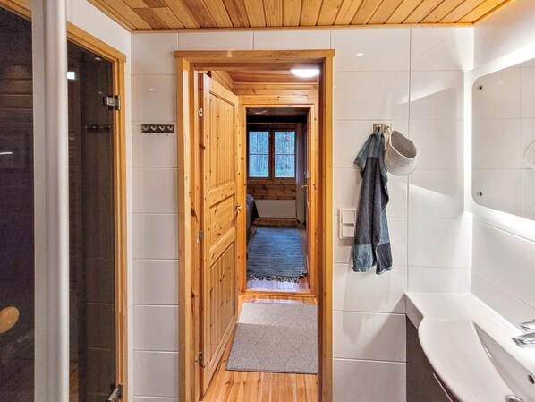 Un pasillo que conduce a un baño con puerta de madera, un perchero y vistas a un bosque por una ventana.
