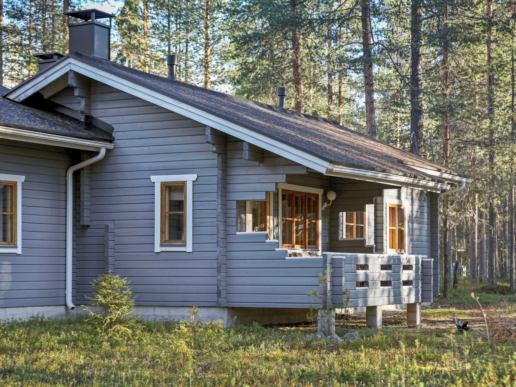 Ett tvåvåningshus med en veranda, en skorsten och en skog som bakgrund.