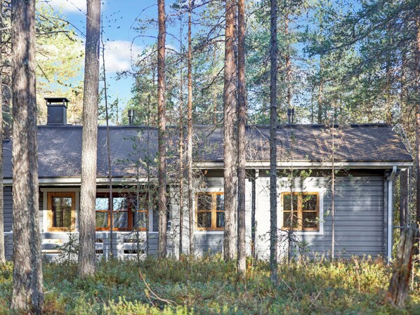 Une cabane entourée de grands arbres, sous un ciel dégagé.