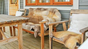A wooden deck with a bench and a table, a window with wooden frames, and a view of a forest. - Purnukka by Interhome (Kuusamo)