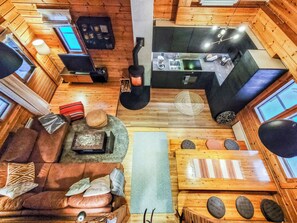 Interior de cabana com sofá, mesa de jantar, cozinha e lareira.