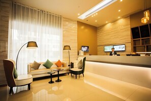 A modern hotel lobby with a reception desk, seating area, and a large window with sheer curtains. - City Comfort Inn (Wuhu)
