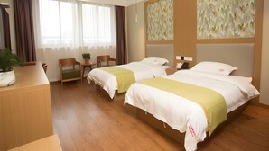 Ein Hotelzimmer mit zwei Betten, einem Schreibtisch, einem Stuhl, einer Pflanze und einem Fenster mit Vorhängen.