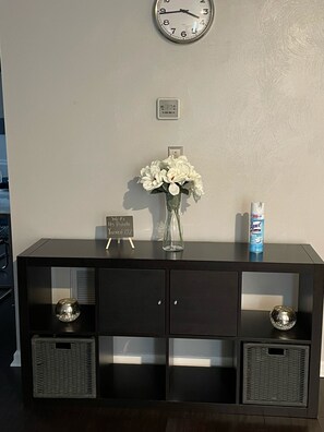 A dark wooden console table with a clock, a vase with white flowers, a sign, and a can of Lysol.