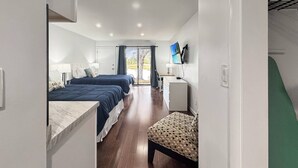 Una camera d'albergo con due letti, una scrivania, una sedia e una televisione appesa al muro.