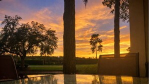 A sunset view from a glass table with a metal ring, surrounded by trees and a clear sky.