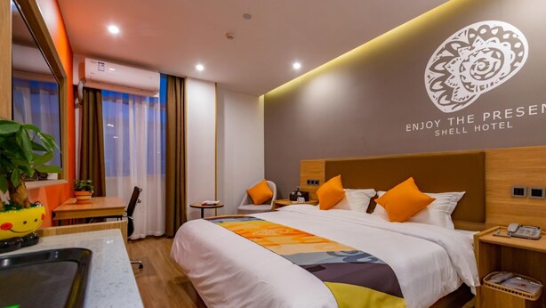 A hotel room with a bed, bedside tables, a desk, a chair, a small table, and a potted plant. - Shell Jiangsu Kunshan Development Zone Wusongjiang South Road Hotel (Suzhou)