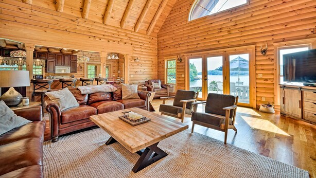 L’intérieur de cette vaste cabane en rondins est chaleureux, avec un salon accueillant, des poutres en bois au plafond et de grandes fenêtres offrant une vue sur le paysage extérieur.