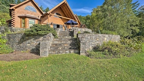 Une cabane en rondins avec un escalier en pierre menant à l’entrée, le tout entouré d’une végétation luxuriante.