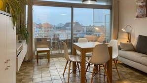 Ein modernes Wohnzimmer mit Essbereich, großen Fenstern und Blick auf Gebäude.