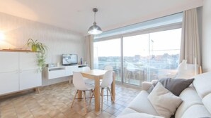 Ein modernes Wohnzimmer mit einer Couch, einem Essbereich mit Tisch und Stühlen, einem Fernseher und einem großen Fenster mit Blick auf die Stadt.