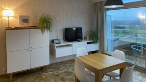 Ein modernes Wohnzimmer mit Fernseher, weißen Schränken, einem Esstisch und Stühlen.