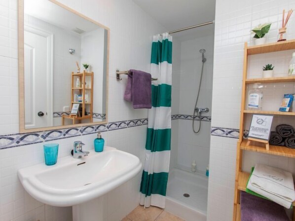 A bathroom with a white sink, a mirror, a shower with a green and white striped curtain, and a shelf with toiletries.