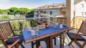 Un balcón con una mesa dispuesta para el desayuno, un cartel de bienvenida y vistas de los edificios y la vegetación circundantes.