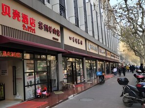 A row of storefronts with signage in a foreign language, a pedestrian walkway, and parked motorcycles. - Shell Shanghai Normal University Hongcao Road Metro Station Guiping Road Hotel (Shanghai)