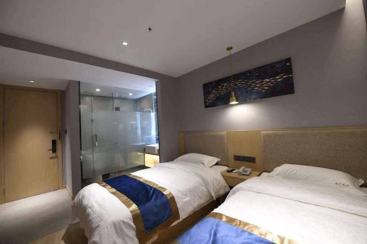 Quarto de hotel com duas camas, box de vidro para o chuveiro e um quadro na parede.