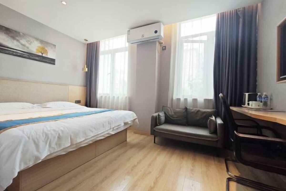 Quarto de hotel com cama, escrivaninha, cadeira e aparelho de ar condicionado.