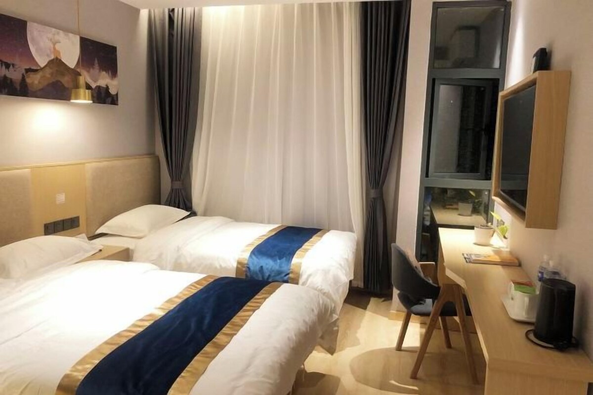 Quarto de hotel com duas camas, uma escrivaninha, uma cadeira, uma televisão e um quadro na parede.