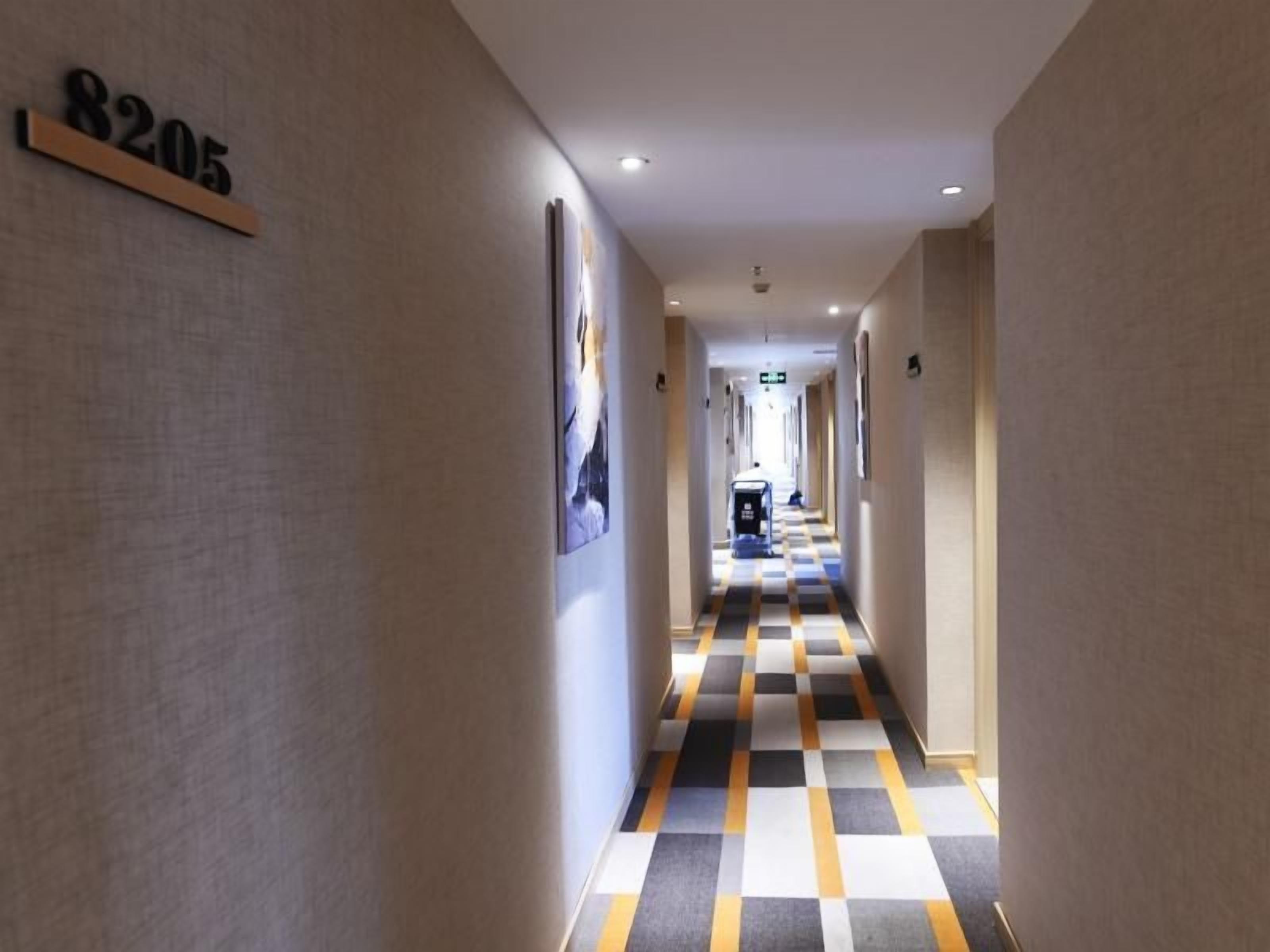 Un couloir d’hôtel avec un sol à carreaux, un panneau indiquant le numéro des chambres sur le mur et des tableaux encadrés accrochés aux murs.