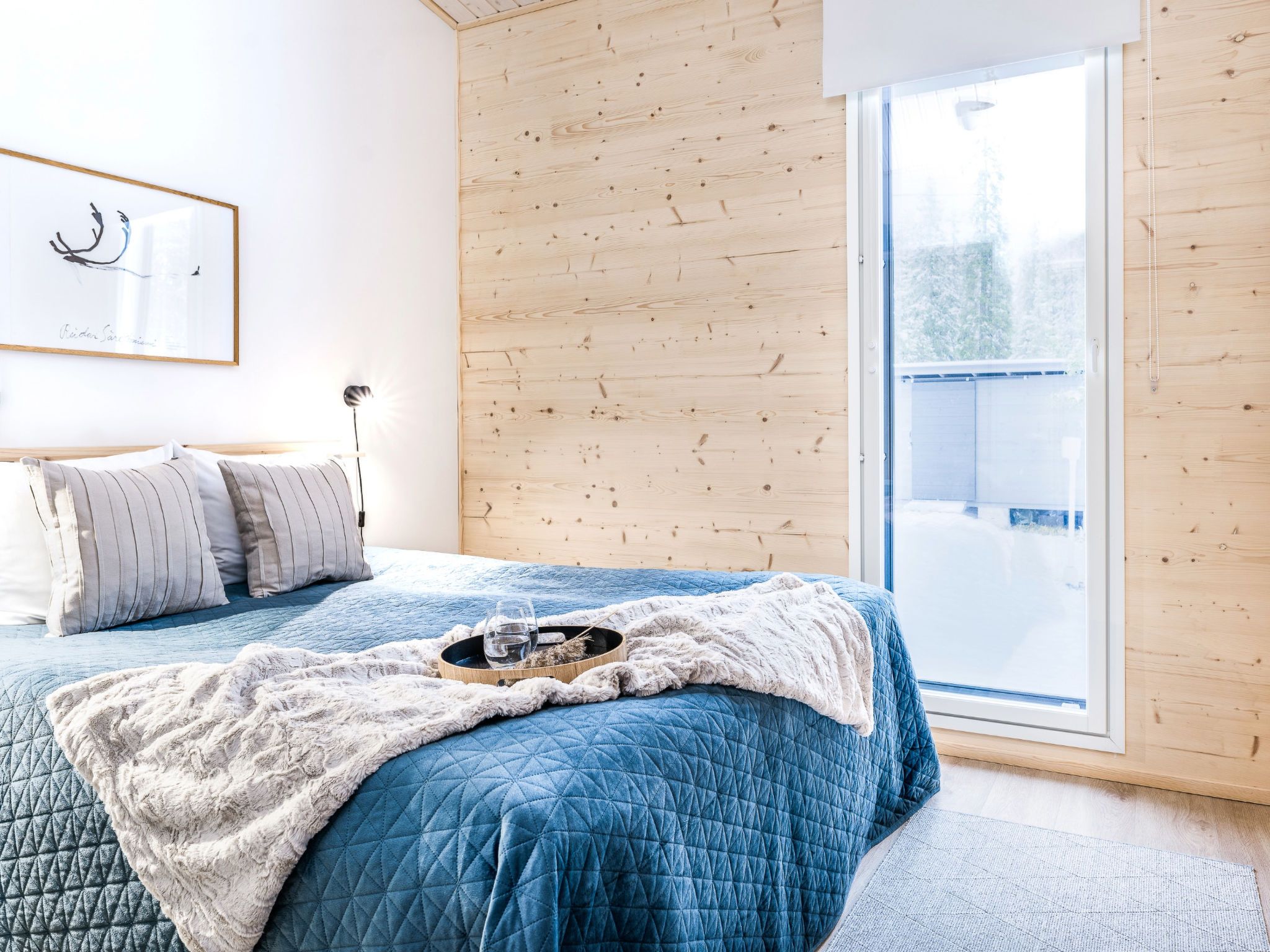 A bedroom with a bed, pillows, a blanket, a framed picture on the wall, and a window with a view of a snowy landscape.