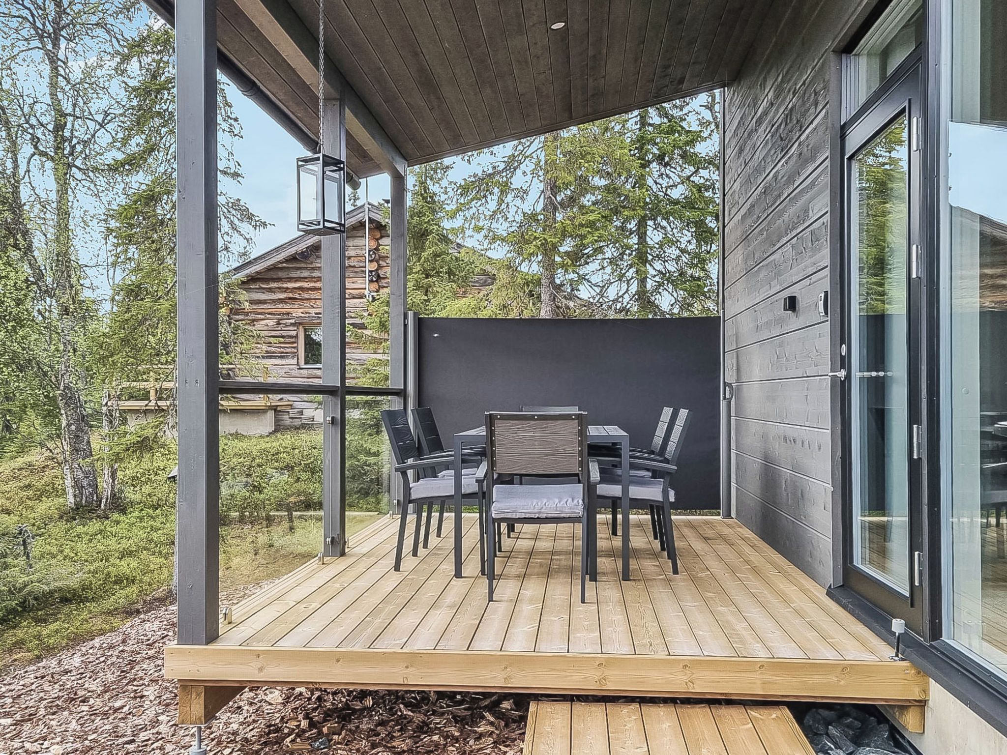 Una terraza moderna al aire libre con una mesa y sillas para comer, rodeada por una cubierta de madera y vistas a una zona boscosa.