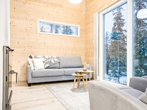 A cozy room with a grey sofa, a small round table, and a large window offering a view of snow-covered trees.