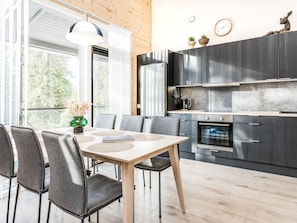 A modern kitchen with dark cabinetry, a built-in oven, and a dining area with a wooden table and grey chairs.
