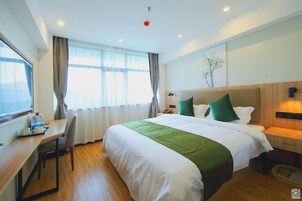 Habitación de hotel con una cama grande, un escritorio con silla, una mesita de noche y una ventana con cortinas.