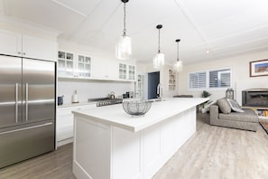 A modern kitchen with white cabinetry, a stainless steel refrigerator, a central island with a wire basket, pendant lighting, and a built-in oven. - Bellavia Forest Retreat with pool and spa. Minutes to lake and beaches! (Whoota)