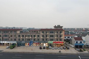 Un edificio de varios pisos con una fila de comercios en la planta baja, un estacionamiento al frente y vistas de edificios residenciales al fondo.