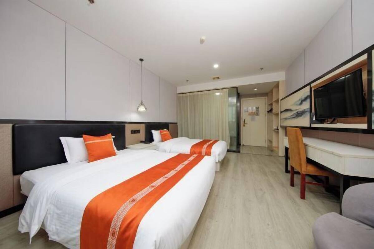 A hotel room with two beds, a desk, a chair, a TV, and a door leading to a bathroom.