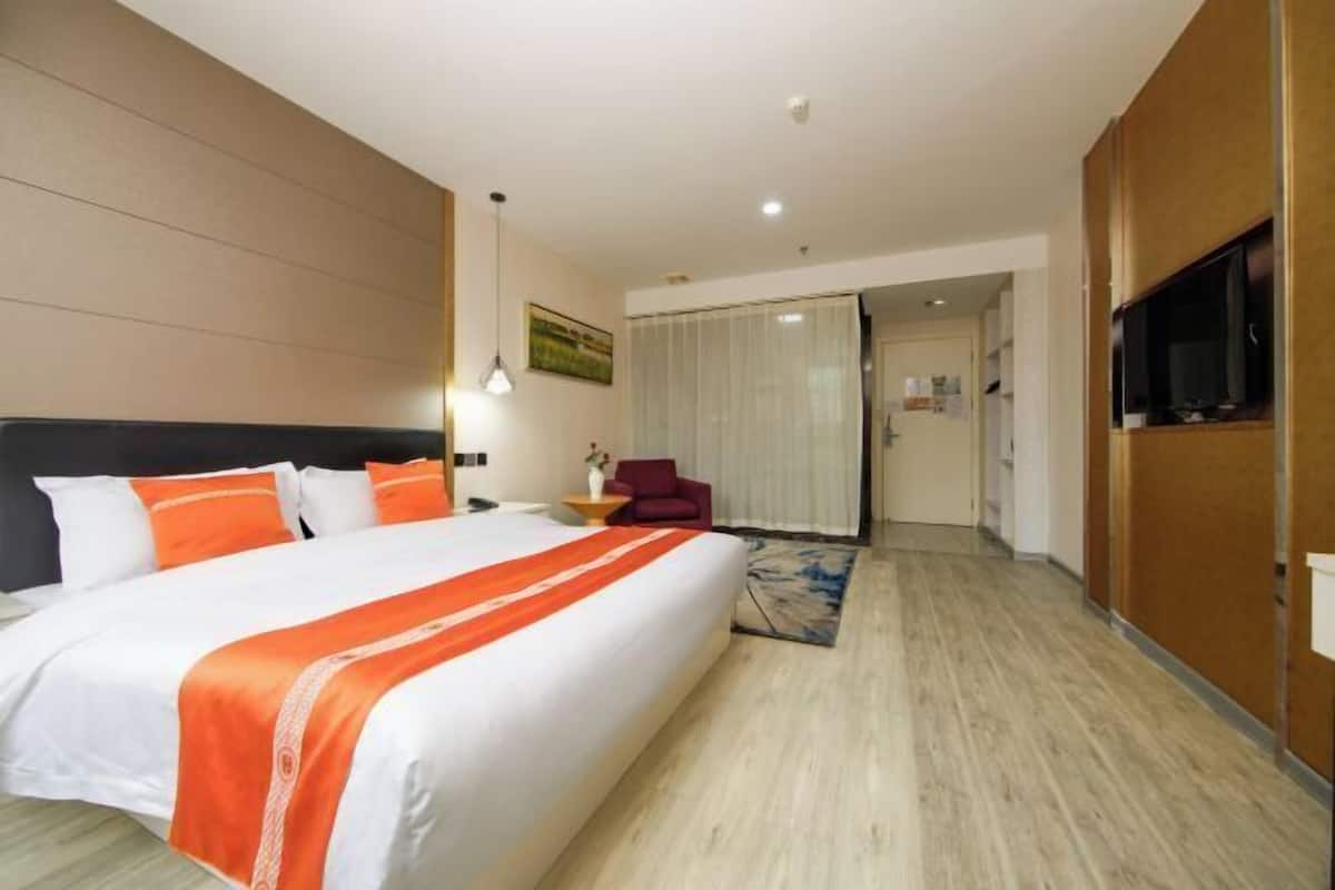 A hotel room with a large bed, a TV, a desk, and a chair.