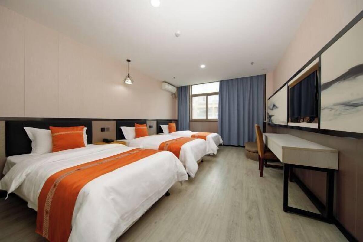A hotel room with two beds, a desk, a chair, a large window with curtains, and a painting on the wall.