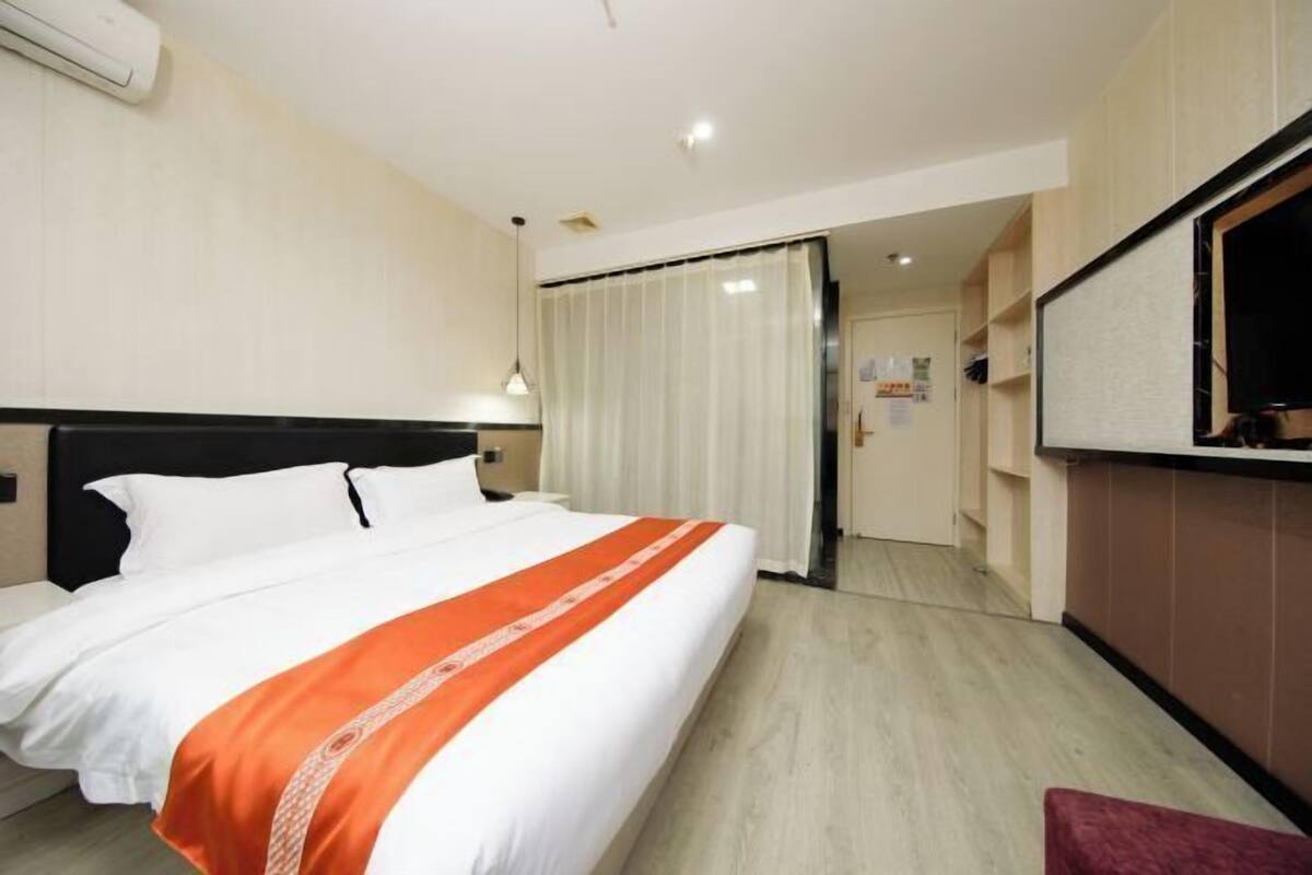 A hotel room with a bed, a TV, a desk, and a bathroom door.