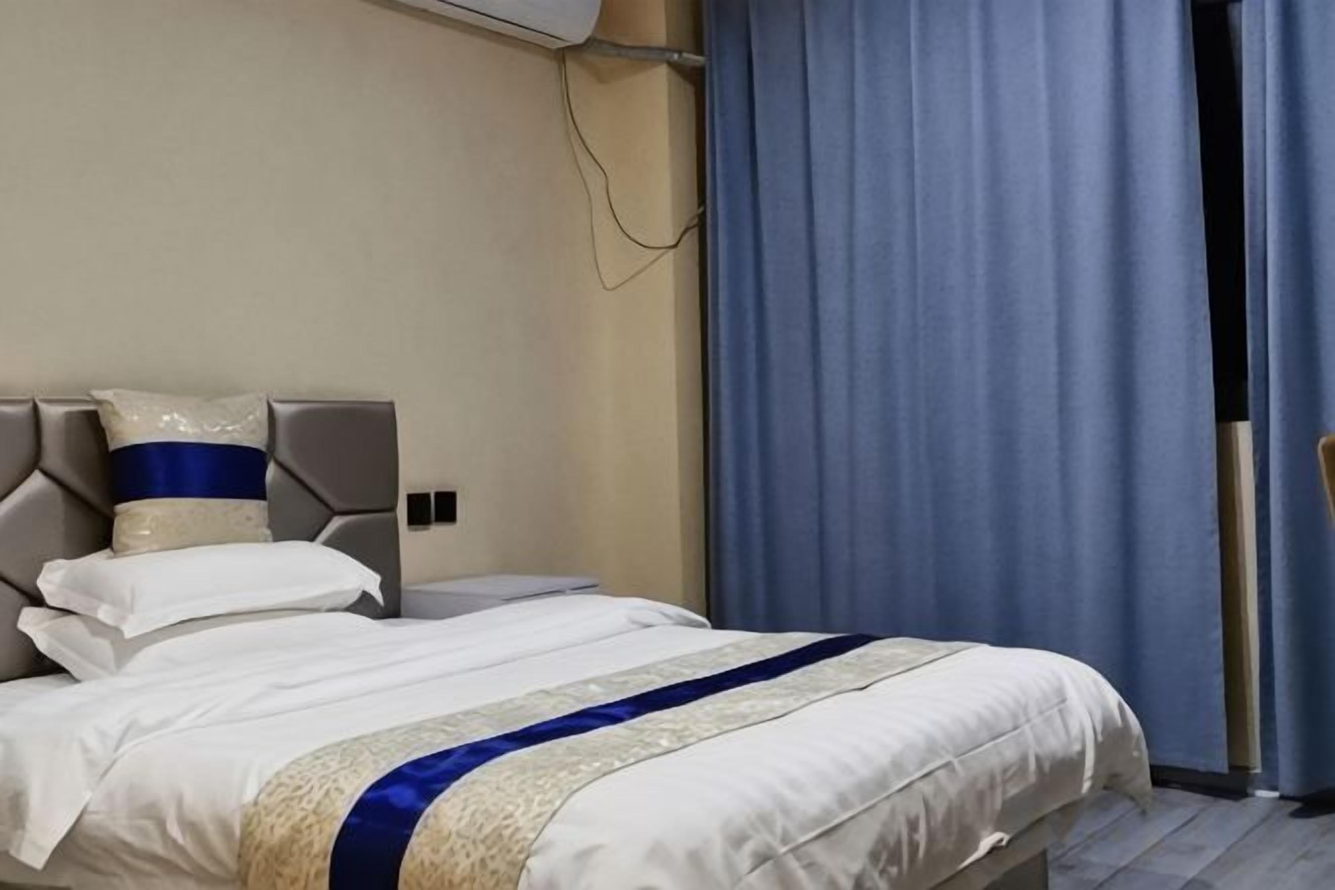 Habitació d'hotel amb un llit, un capçal, una finestra amb cortines i un aire condicionat fixat a la paret.