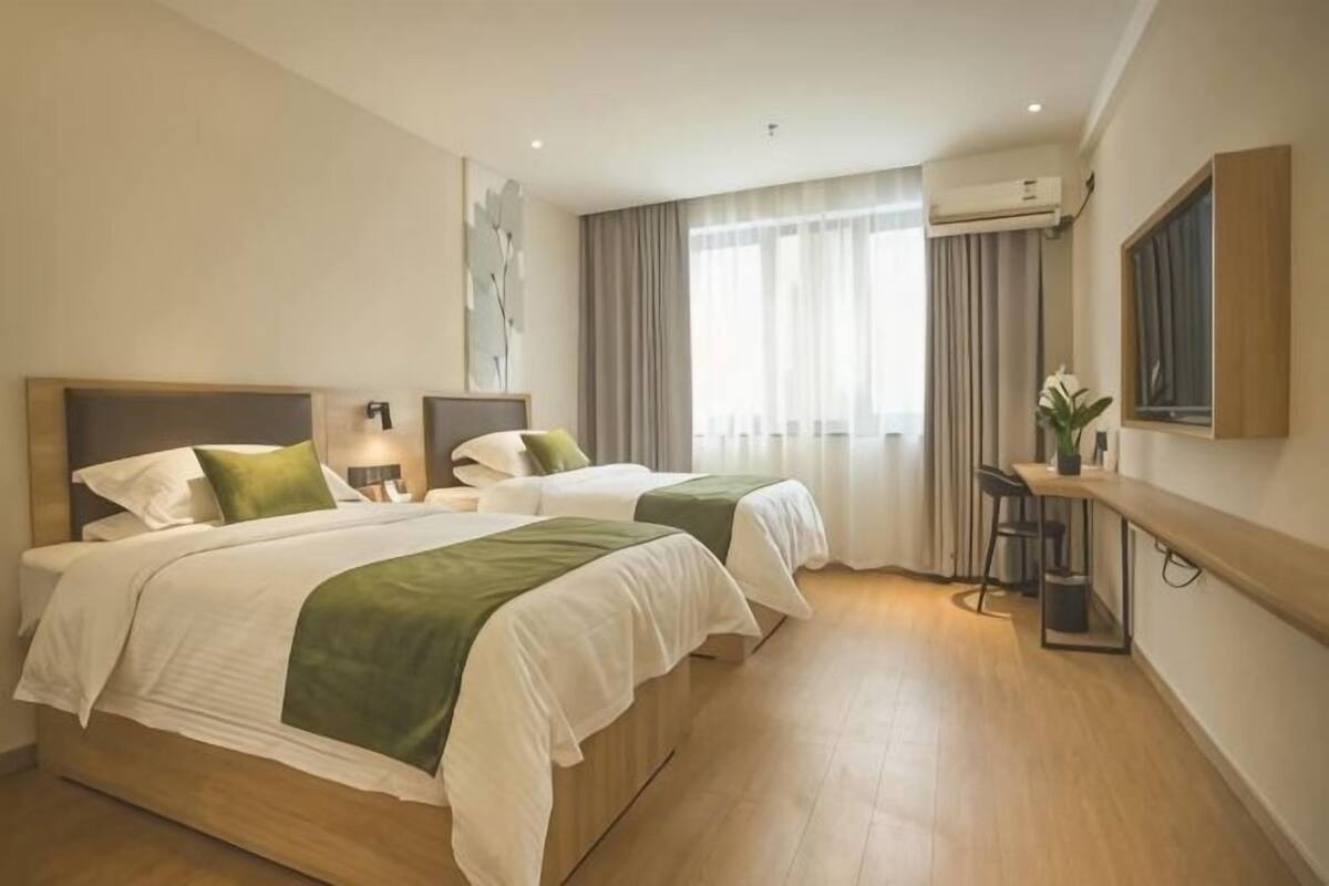 Een hotelkamer met twee bedden, een bureau, een stoel en een raam met gordijnen.