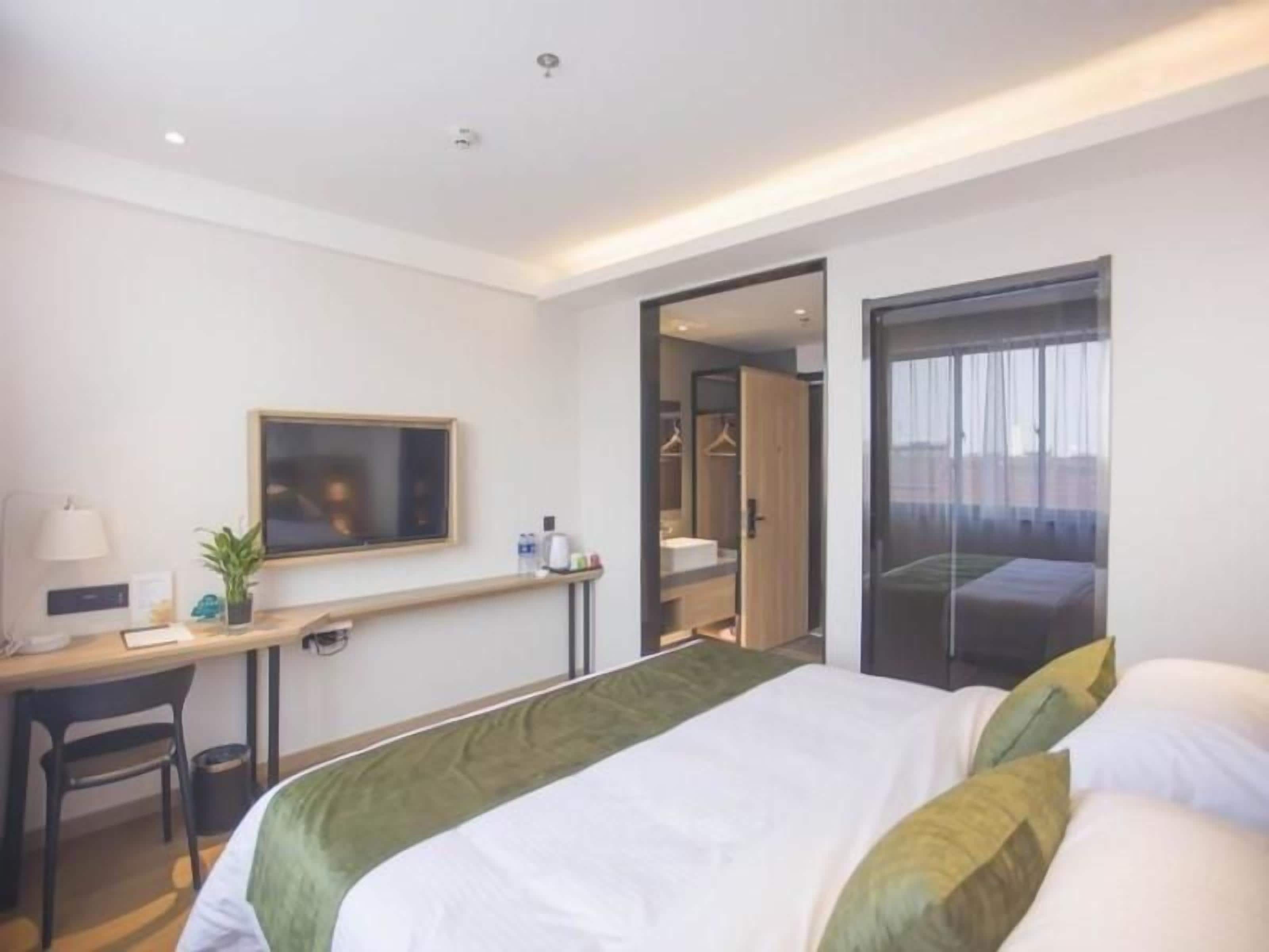 A hotel room with a bed, a desk, a chair, a TV, and a wardrobe.
