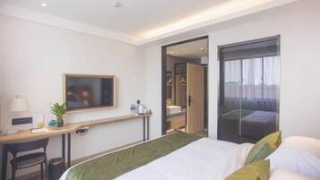 A hotel room with a bed, a desk, a chair, a TV, and a wardrobe.